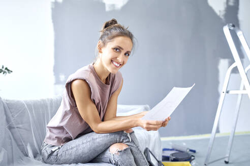 Smiling woman reading paper while sitting on sofa at home - BSZF01755