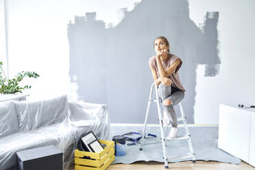 Thoughtful woman with head in hands sitting on ladder against wall at home - BSZF01757