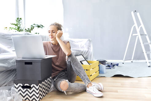 Smiling woman using laptop while sitting by sofa at home - BSZF01758