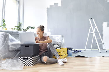 Lächelnde Frau arbeitet am Laptop, während sie zu Hause auf dem Sofa sitzt - BSZF01759
