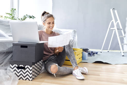 Young woman holding paper while working on laptop at home - BSZF01760