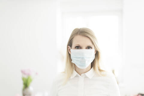 Blond woman wearing protective face mask while standing at office stock photo