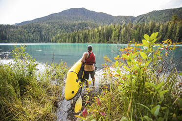 Ein Mann trägt ein aufblasbares Ruderboot (Kajak) in den Cheakamus Lake in Whistler. - CAVF89900