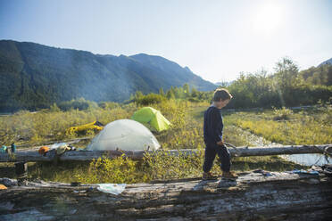 Young boy balancing on fallen log near wilderness campsite, Canada. - CAVF89908