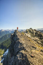 Bergsteiger steht auf dem Gipfel eines felsigen Berggipfels, B.C. Kanada - CAVF89977