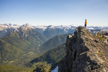 Man on mountain summit looking out at view of forest and peaks. - CAVF89979