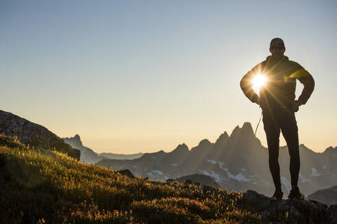 Sun shines through arm of silhouetted hiker on mountain ridge - CAVF89988