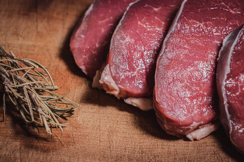 Teilstücke von argentinischem Rindfleisch auf Holzbrettchen zusammen mit Rosmarin - CAVF90002