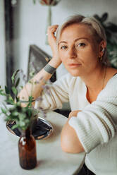 Blond woman with short haircut sitting at table, looking at camera - CAVF90016