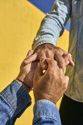 Gay man putting ring in young man finger while standing by yellow wall - VEGF03048