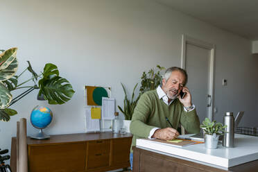 Älterer Mann, der bei der Arbeit zu Hause mit seinem Handy telefoniert - VABF03618