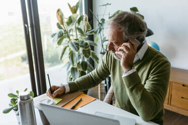 Älterer Mann, der bei der Arbeit zu Hause mit seinem Handy telefoniert - VABF03619