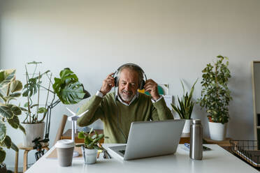 Lächelnder Mann mit Kopfhörern bei der Arbeit am Laptop zu Hause - VABF03626