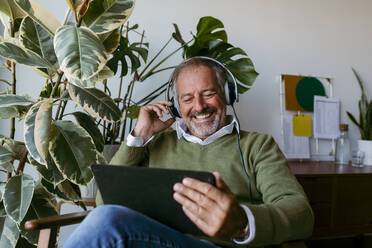 Lächelnde reife Männer mit Kopfhörern bei der Nutzung eines digitalen Tablets zu Hause - VABF03642