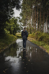Rear view of woman walking on wet footpath during rainy season - DMGF00223