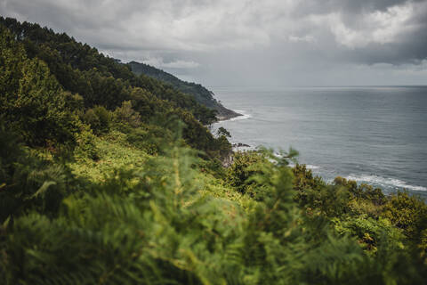 View of sea by mountain against cloudy sky during rainy season stock photo