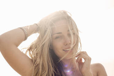 Junge Frau mit Hand in den Haaren, während sie an einem sonnigen Tag am Strand steht - AJOF00414