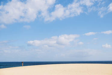 Entfernte Ansicht einer jungen Frau am Strand an einem sonnigen Tag - DGOF01560