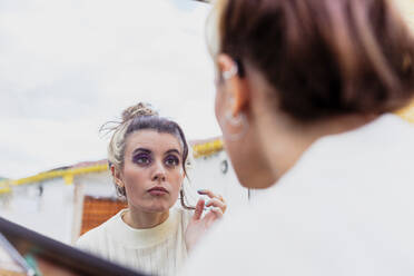 Young woman looking in mirror outdoors - MRRF00584