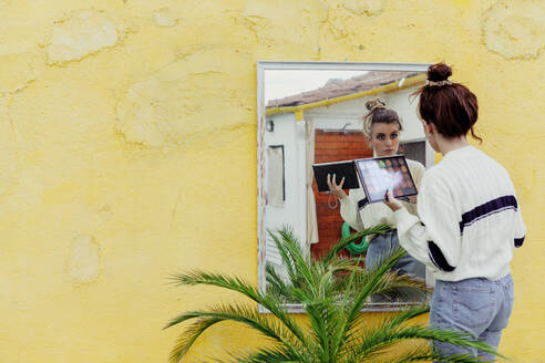 Young woman looking at mirror with make up palette standing in back yard - MRRF00585