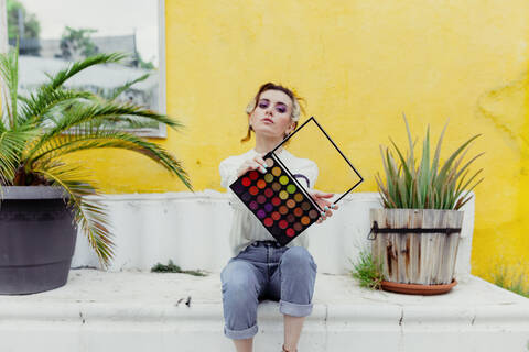 Schöne Frau sitzt mit Make-up-Palette im Hinterhof, lizenzfreies Stockfoto