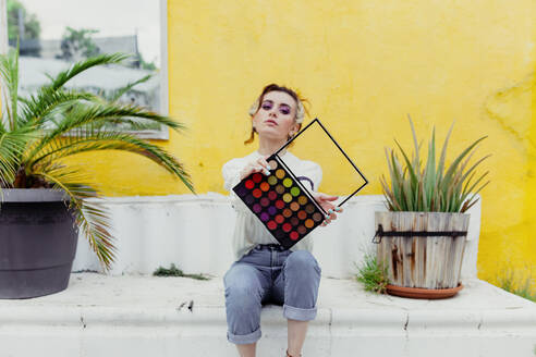 Beautiful woman sitting with make up palette in back yard - MRRF00588