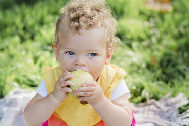 Niedliche Baby-Mädchen essen Obst, während auf Gras im Park sitzen - NMSF00424