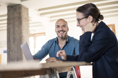 Mann lächelnd bei der Arbeit am Laptop mit Frau im Büro - MOEF03472