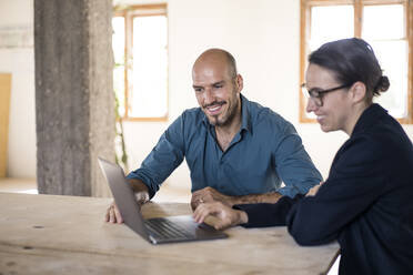 Businessman and woman smiling while working on laptop at office - MOEF03475