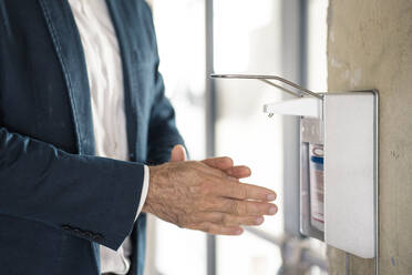 Geschäftsmann wäscht Hände mit Desinfektionsmittel, während er im Büro steht - MOEF03486