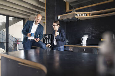 Business people using mobile phone while drinking coffee at office - MOEF03494