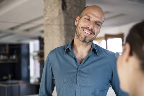 Smiling businessman looking at colleague while standing at office - MOEF03525