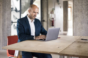 Geschäftsmann im Anzug mit Laptop bei der Arbeit im Büro - MOEF03542