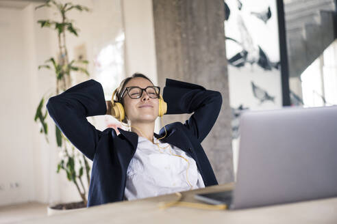 Smiling businesswoman listening music while relaxing on chair at office - MOEF03550