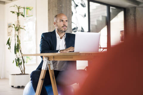 Man wearing suit looking away while sitting by table at office stock photo