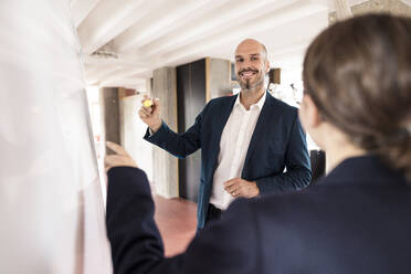 Geschäftsleute diskutieren, während sie im Büro auf ein Whiteboard schreiben - MOEF03565