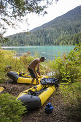 Man on lakeshore, preparing his boats for a packrafting trip at lake. - CAVF90028