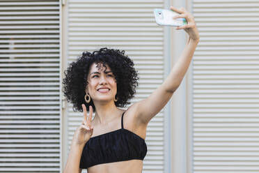 Junge Frau nimmt Selfie auf Smartphone stehend gegen Metallwand - PNAF00004