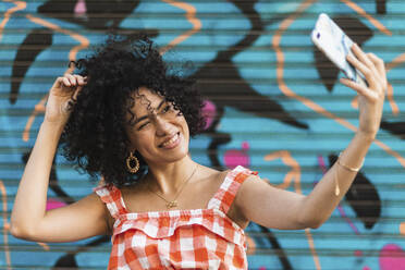 Junge Frau nimmt Selfie auf Smartphone stehend gegen Kunstwand - PNAF00020
