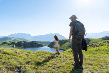 Vater und Tochter stehen auf einer Wiese und schauen auf einen See an einem sonnigen Tag - GEMF04302