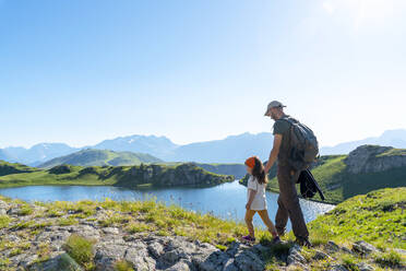 Father and daughter walking on meadow during sunny day - GEMF04303