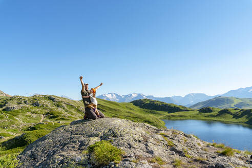 Father kneeling with arms raised with daughter on sunny day against clear sky - GEMF04305