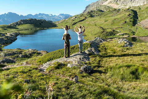 Mutter und Vater, die ihre Töchter auf den Schultern tragen und die Aussicht genießen, während sie an einem sonnigen Tag stehen, lizenzfreies Stockfoto