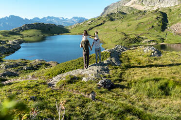 Mother and father carrying daughters on shoulders looking at view during summer - GEMF04314