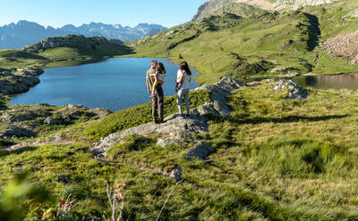 Vater und Mutter tragen ihre Töchter, während sie an einem sonnigen Tag am Seeufer die Aussicht genießen - GEMF04317