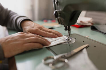 Close-up of hand making protective face mask on sewing machine at home - MRRF00599