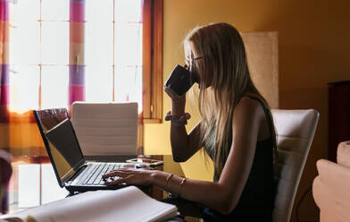 Mädchen benutzt Laptop und trinkt zu Hause Kaffee - MGOF04591