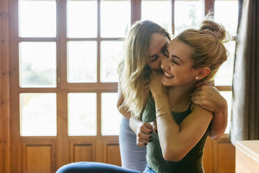 Affectionate mother kissing blond teenage daughter on cheek at home - MGOF04612