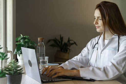 Young female doctor using laptop during online consultation at home office - AFVF07376