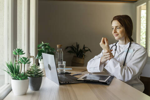 Young female doctor holding wrist while explaining during online consultation at home office stock photo